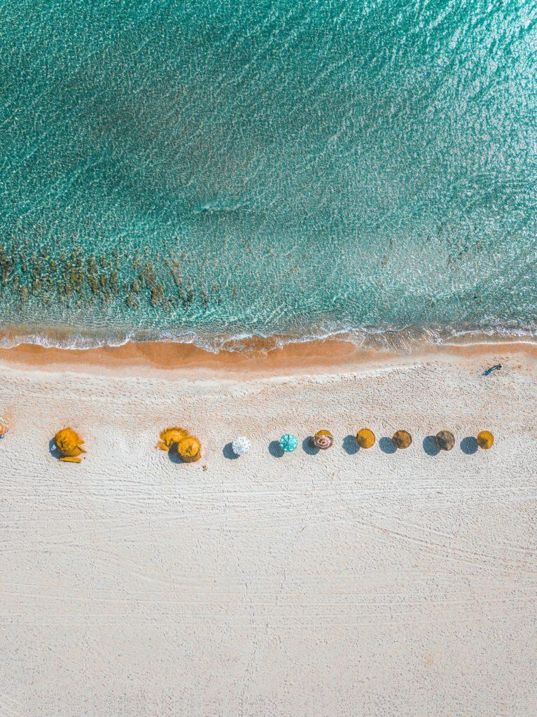 Overhead view of a beach shore with beach umbrellas lined up.